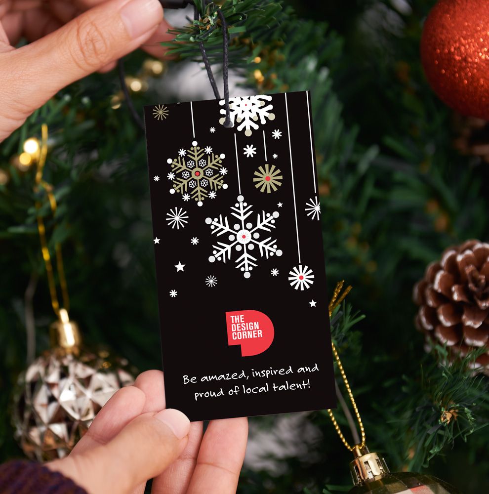 Black Christmas swing tag with snowflakes and The Design Corner logo, hung on a tree